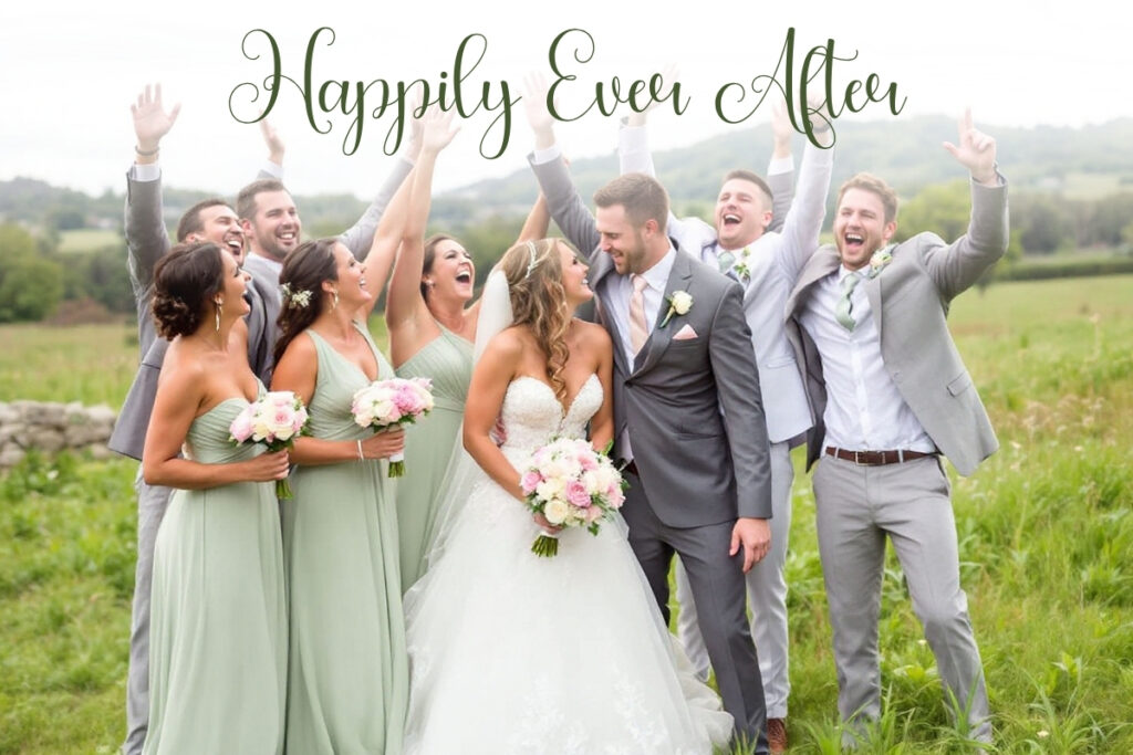 Outdoor wedding party photo with bride in white gown and groom in gray suit surrounded by bridesmaids in light green dresses and groomsmen in gray suits, all celebrating joyfully under 'Happily Ever After' lettering.
