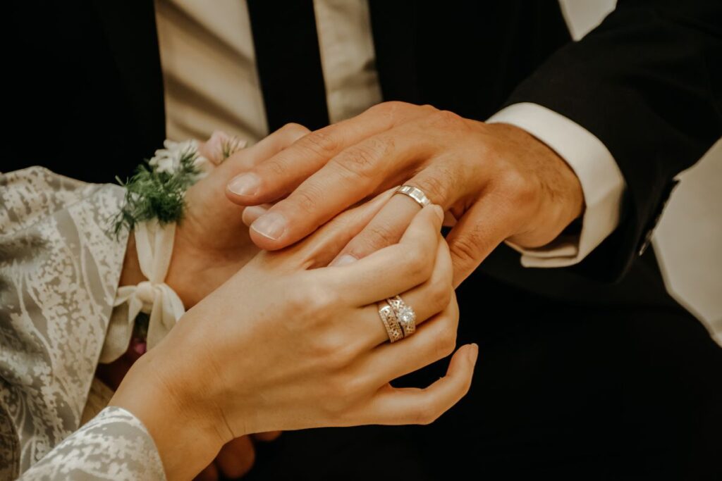 Close-up of two hands wearing wedding rings, one with a simple band and the other with a gemstone ring, gently touching to symbolize love, union, and commitment.
